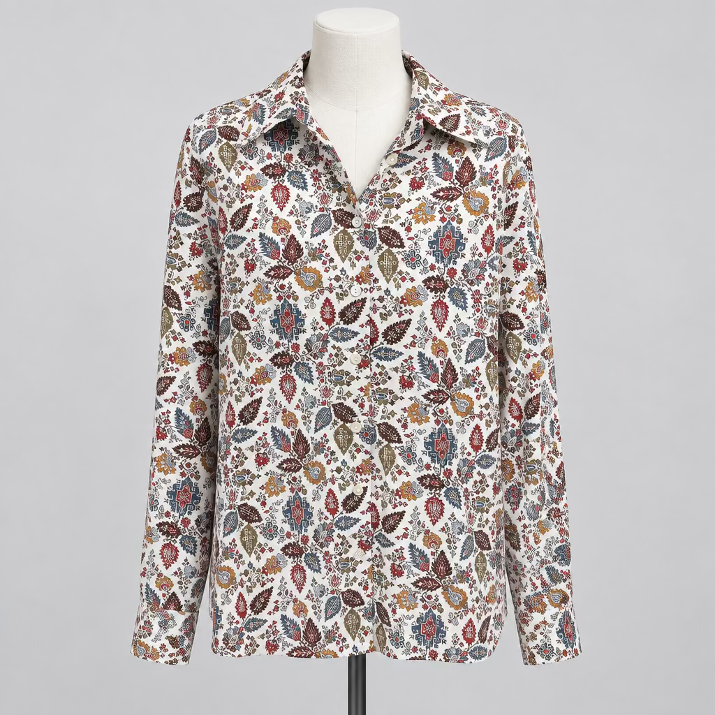 A long-sleeve button-up shirt with an intricate multicolor paisley pattern on a cream base, displayed on a white mannequin torso inside a boutique.
